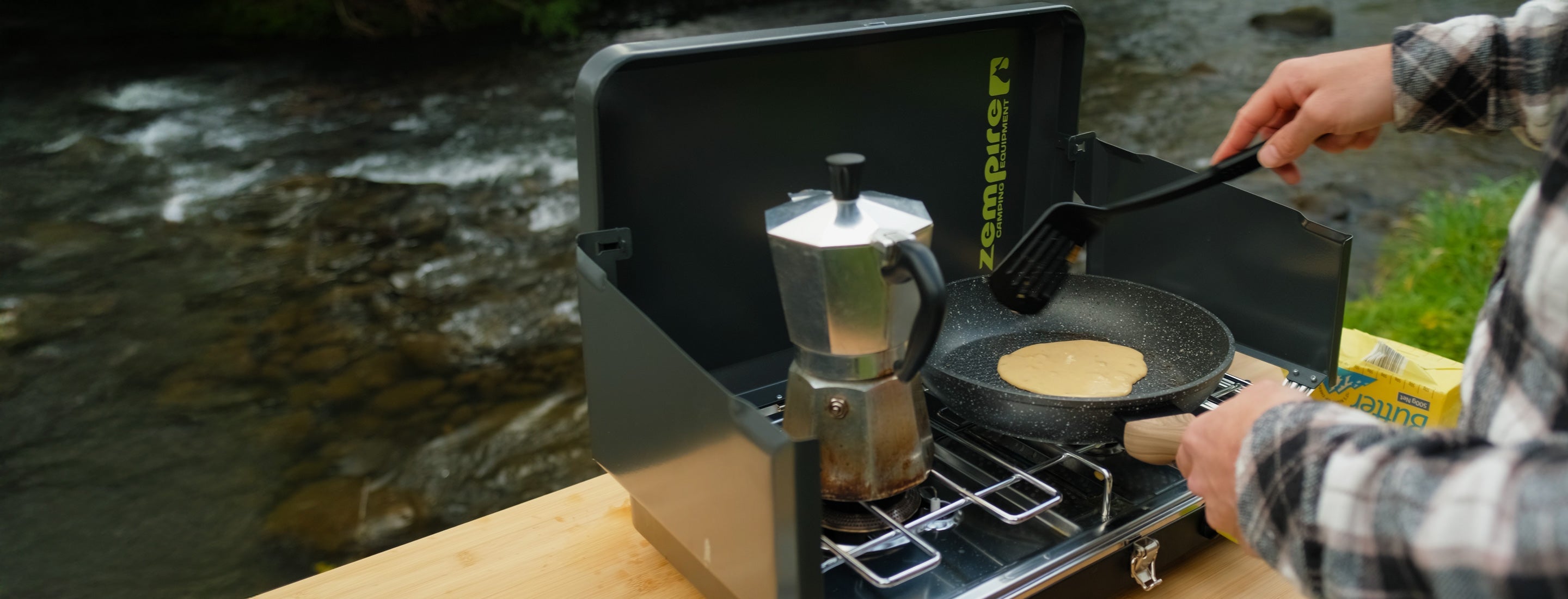 Camping stove with coffee maker and frying pan by a river