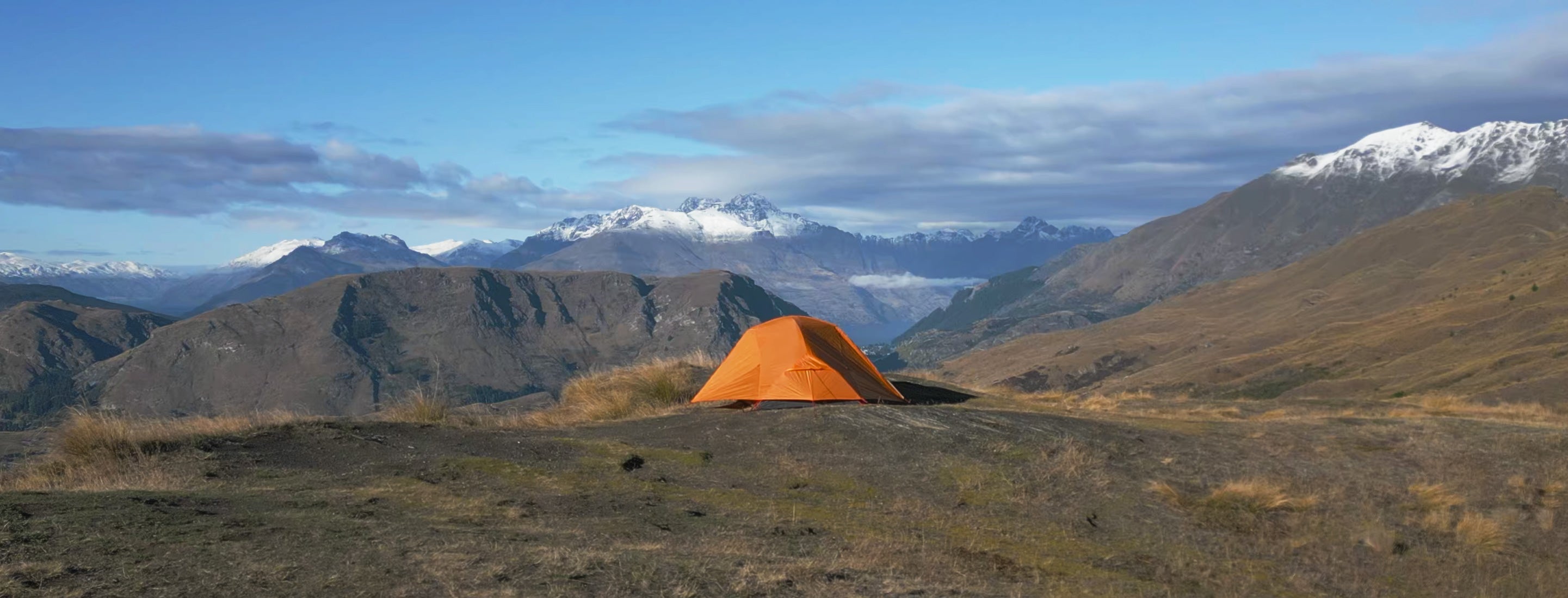 Orange tent in a mountainous landscape with snow-capped peaks.