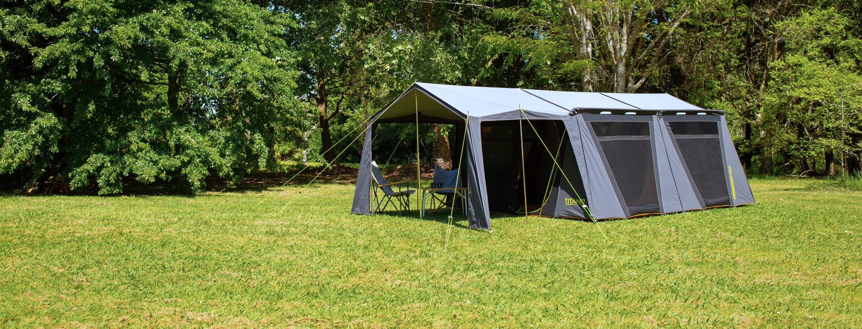 Outdoor canvas pole tent set up in a grassy area with trees in the background